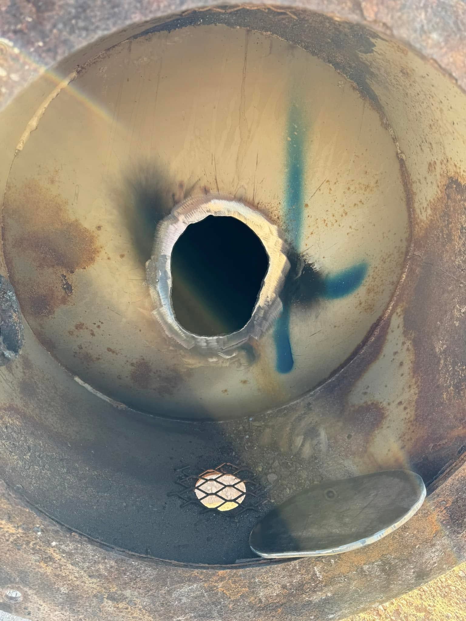 Rusty metal funnel with a central hole and blue paint marks on the inner surface