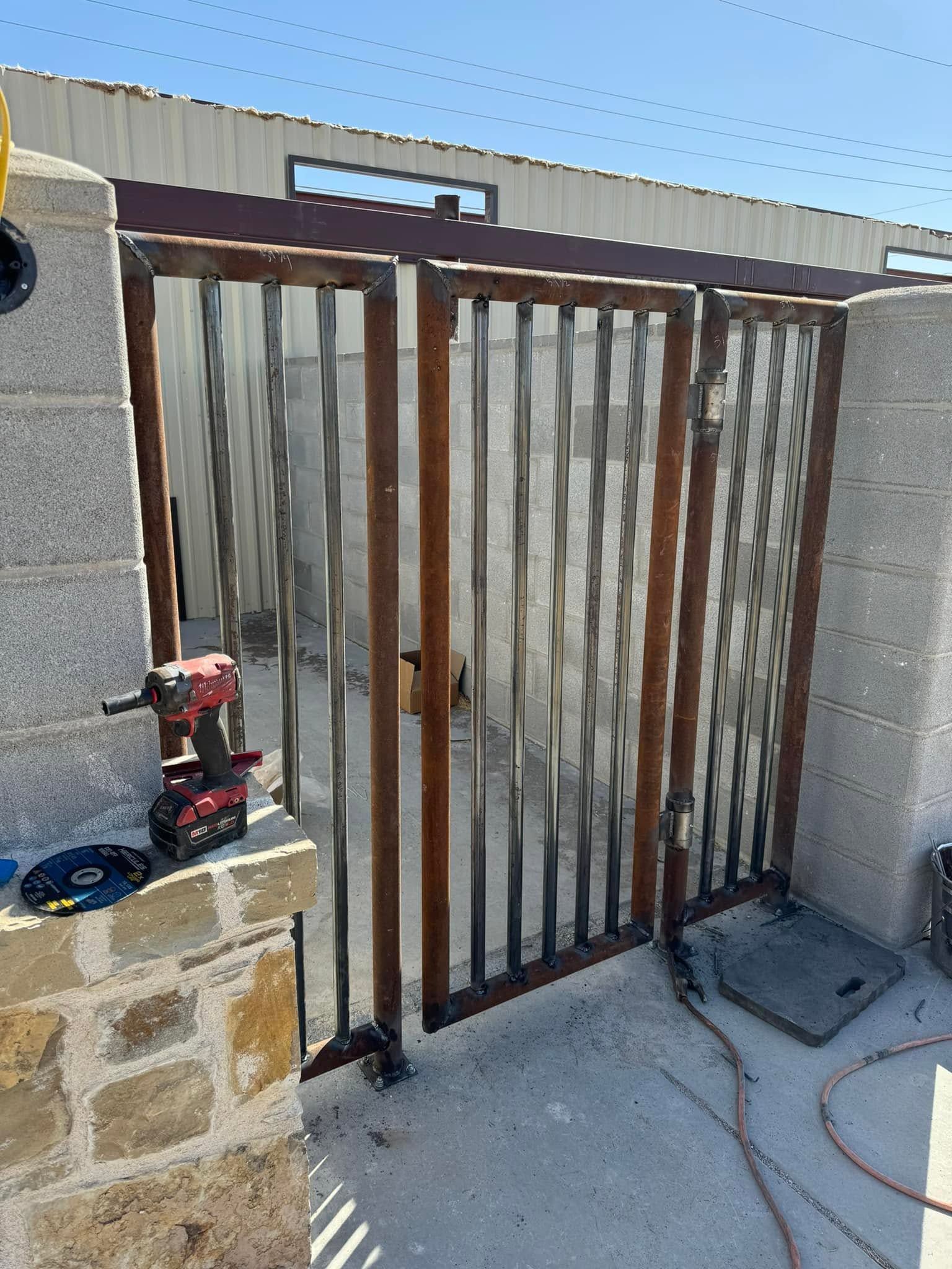 Outdoor metal gate in a stone wall, partly open, with a red and black toy vehicle nearby.