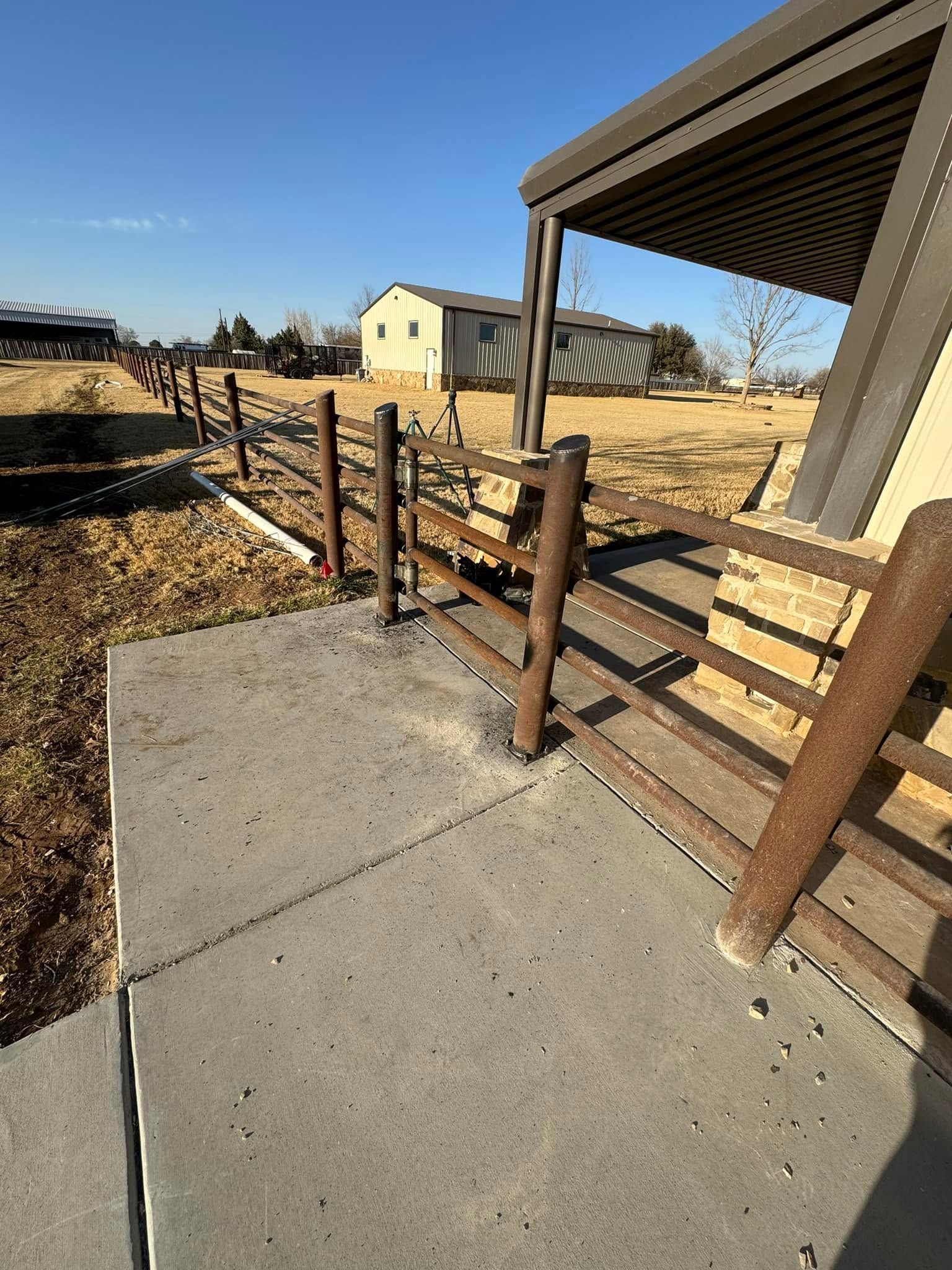 Concrete sidewalk beside a brown metal gate and carport in a dry suburban yard