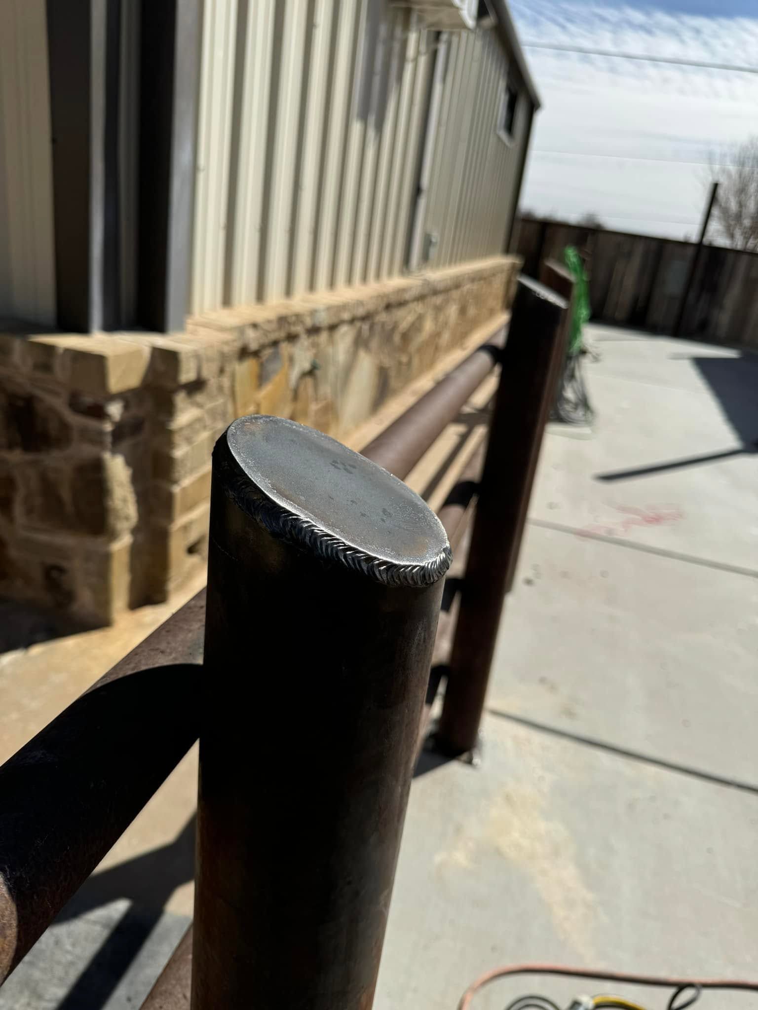 Black metal post beside a sunlit sidewalk next to a beige building and fence