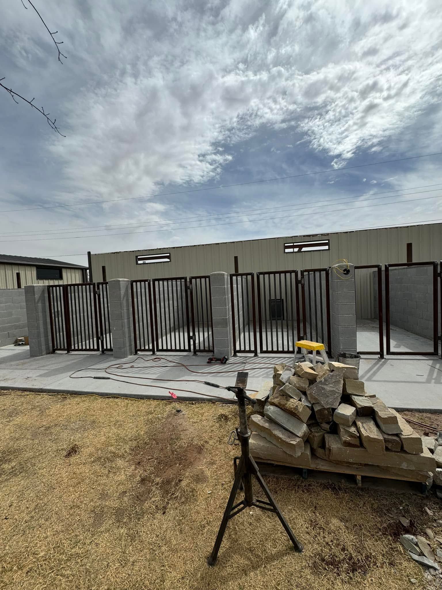 Empty patio with black metal gates, concrete wall, and stacked stones under a cloudy sky