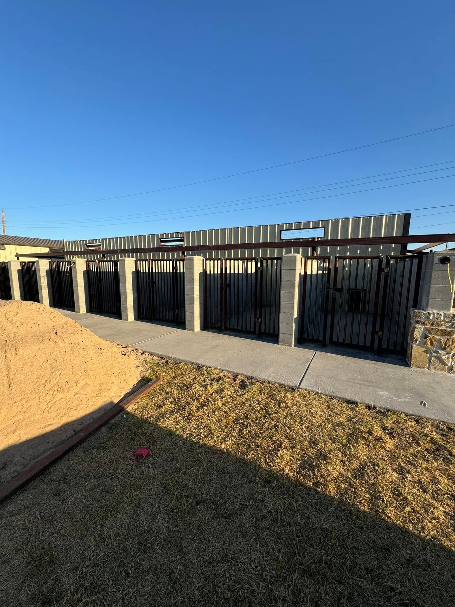 Backyard with black metal fence, tan buildings, and blue sky over grass and gravel path