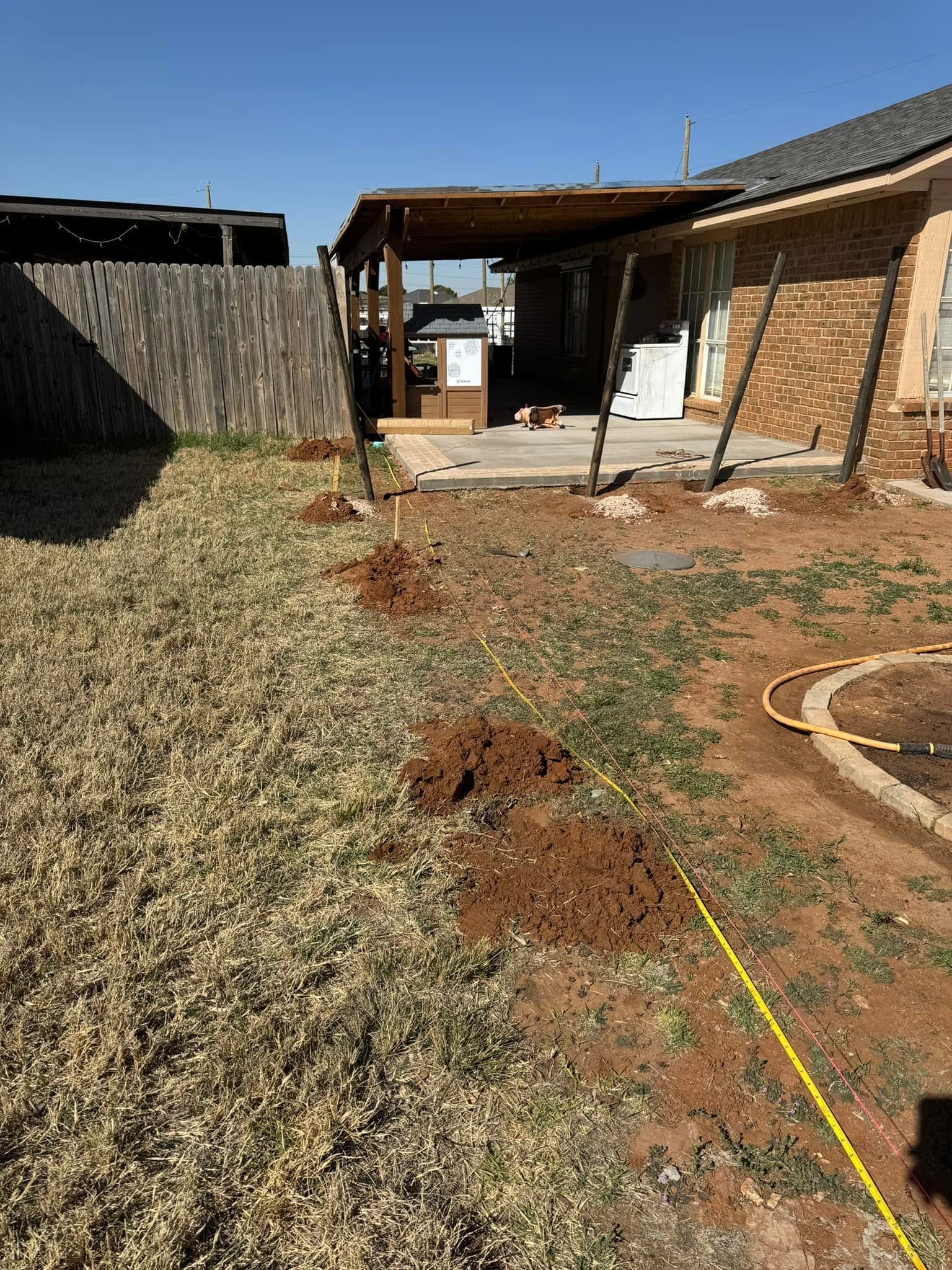 Backyard with dry grass, dirt patches, a brick house patio, and a fenced yard under bright sun