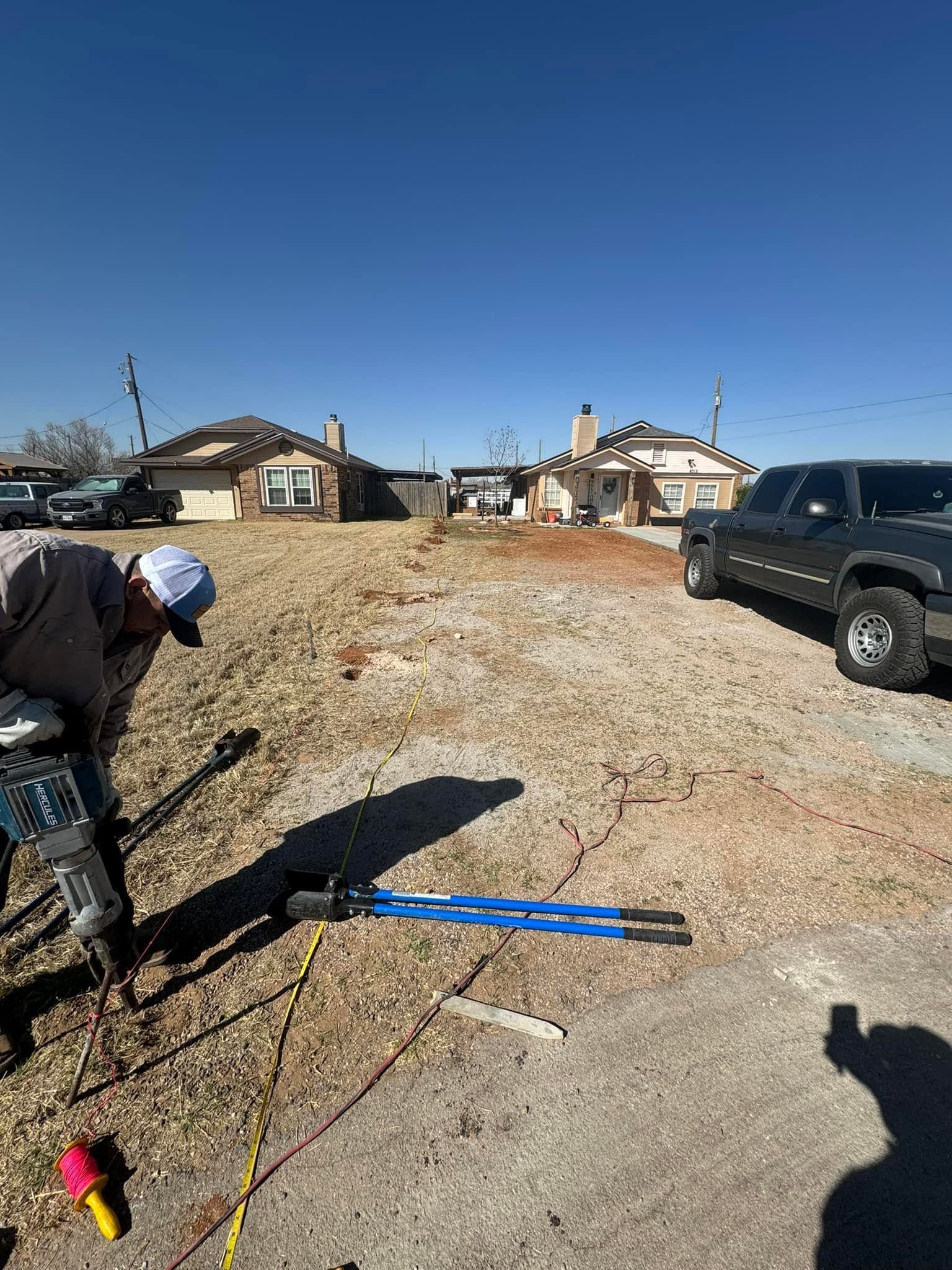 Worker handling tools beside a black SUV on a gravel lot near houses under a clear blue sky