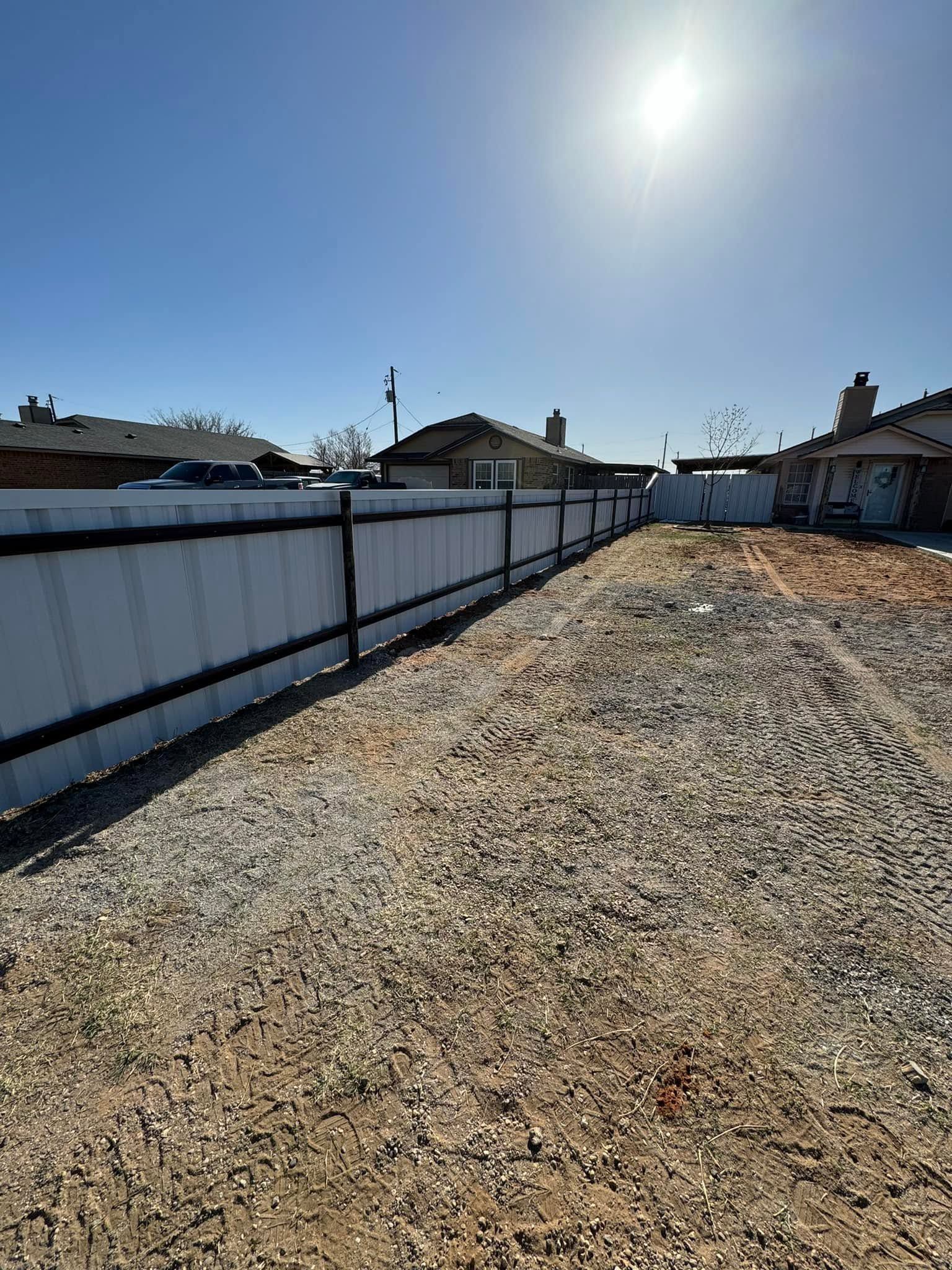 Gravel backyard beside white fences and houses under a bright sun and clear sky