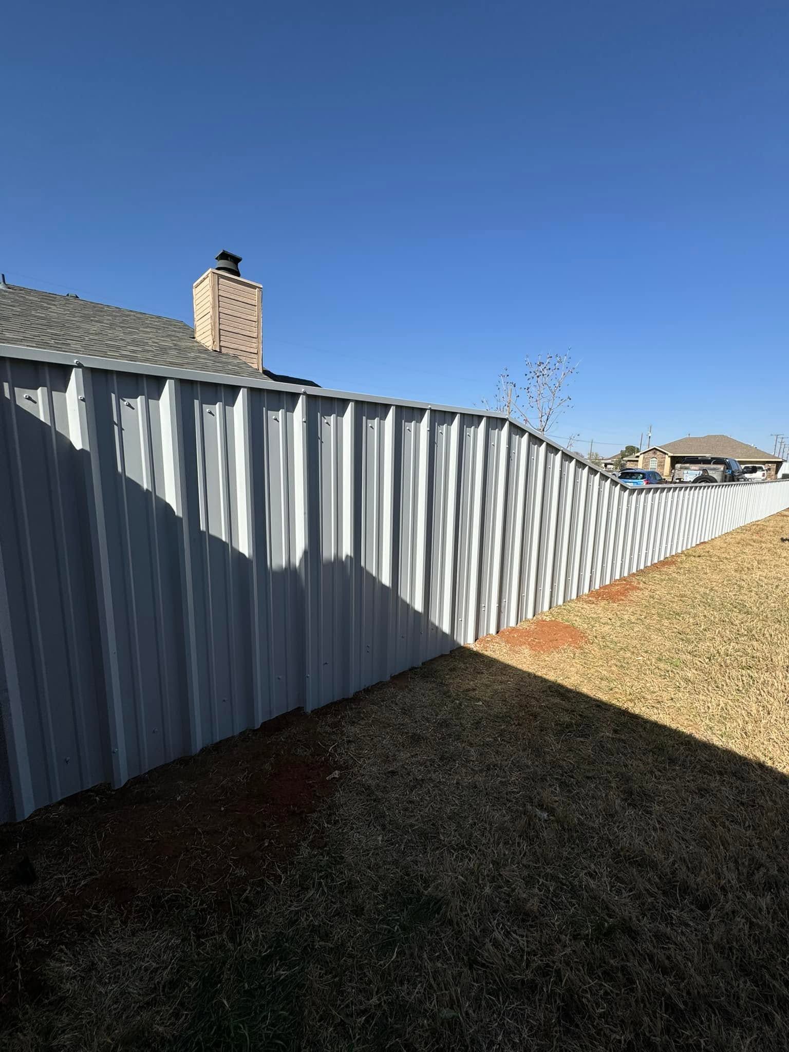Long corrugated metal fence along a sloped yard under a clear blue sky