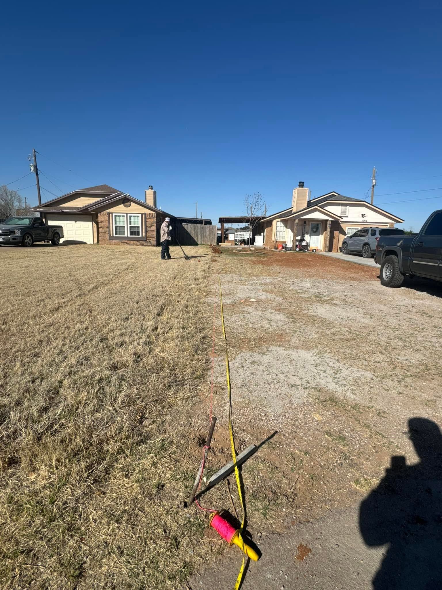 Rural dirt lane between mobile homes with parked trucks under a clear blue sky, yellow tape in the foreground