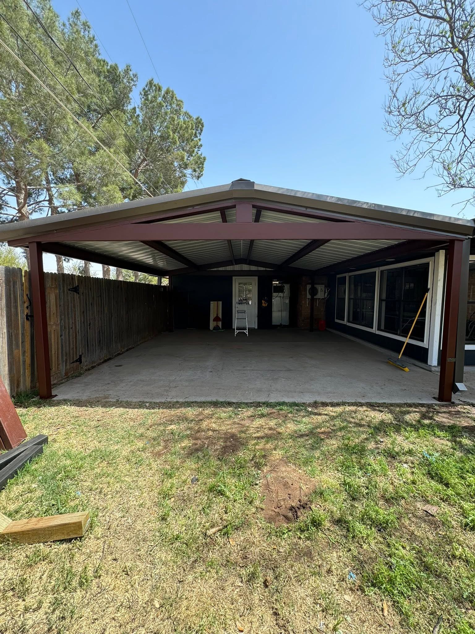 Open carport with concrete floor, metal roof, and trees around a grassy yard