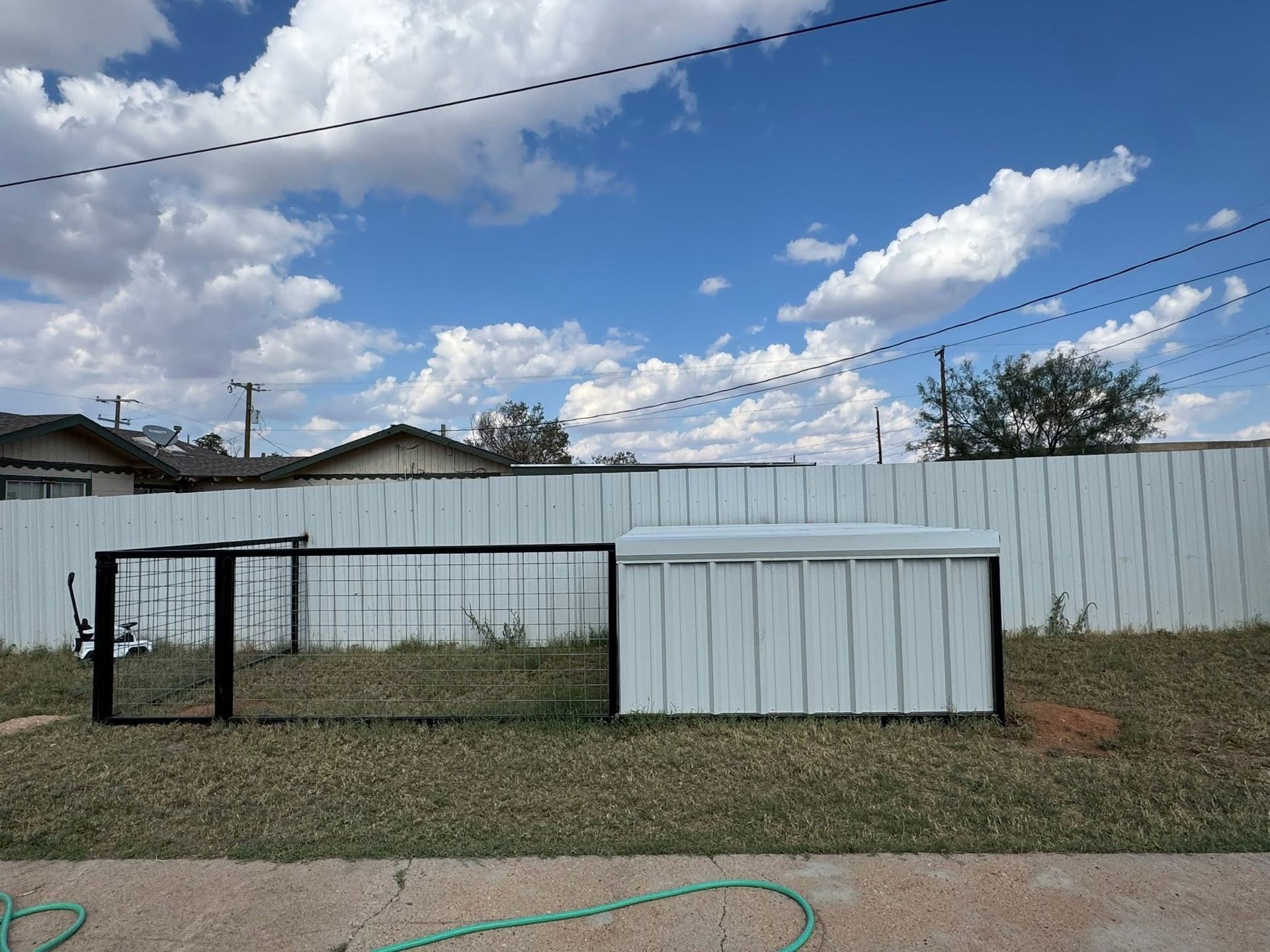Backyard with two small metal structures in front of a white fence under a blue, cloudy sky