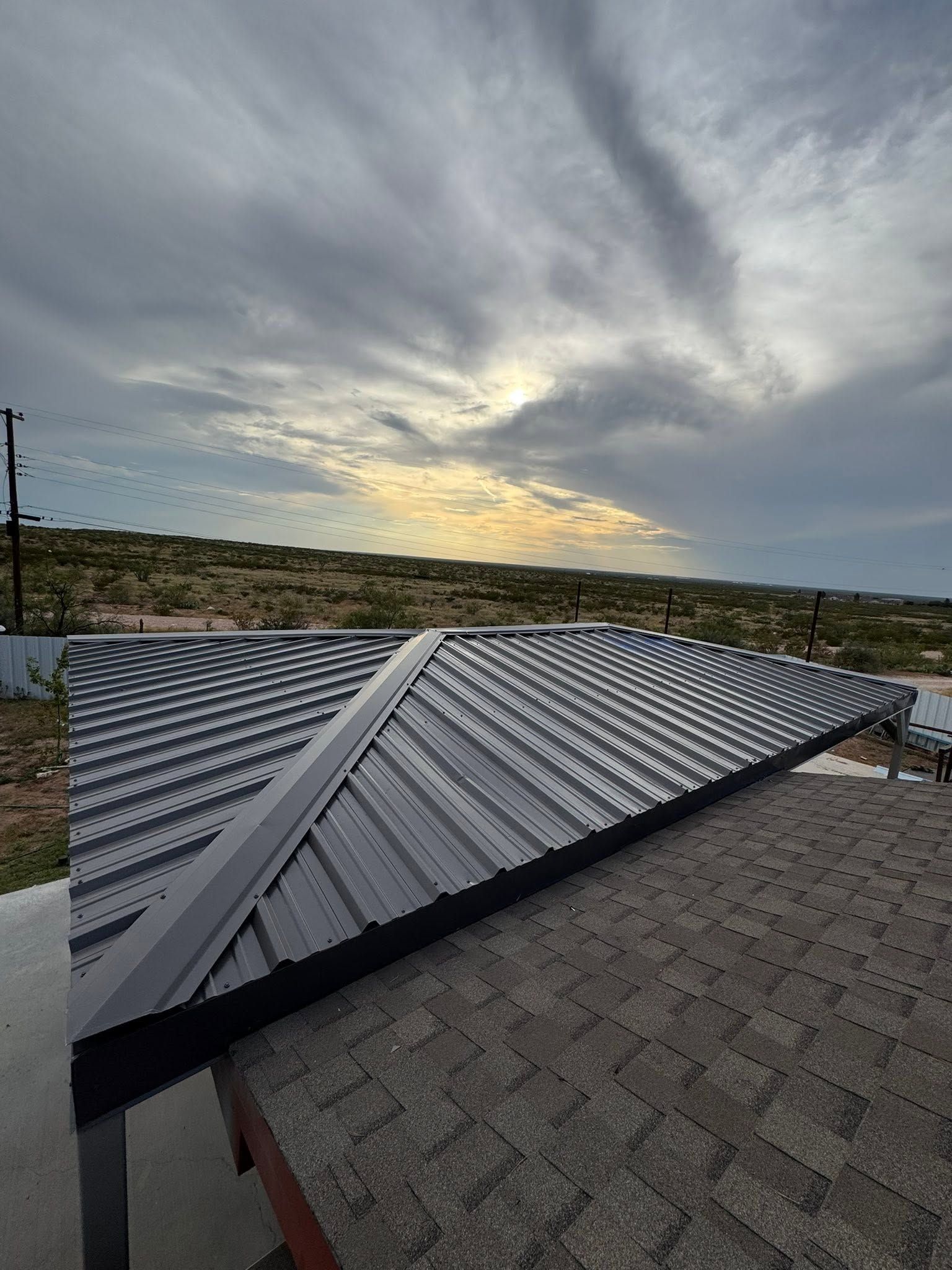 Corrugated metal roof under a cloudy sunset sky, with distant hills and a paved foreground