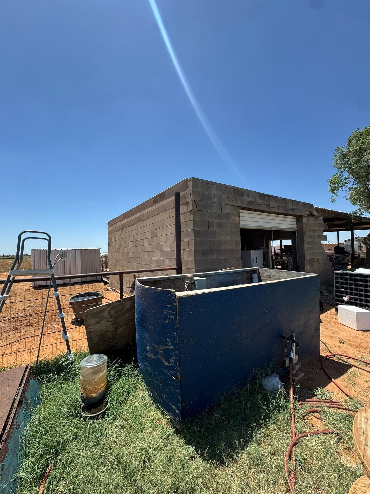 Backyard construction site with a brick building, blue tank, and metal scaffolding under a clear sky