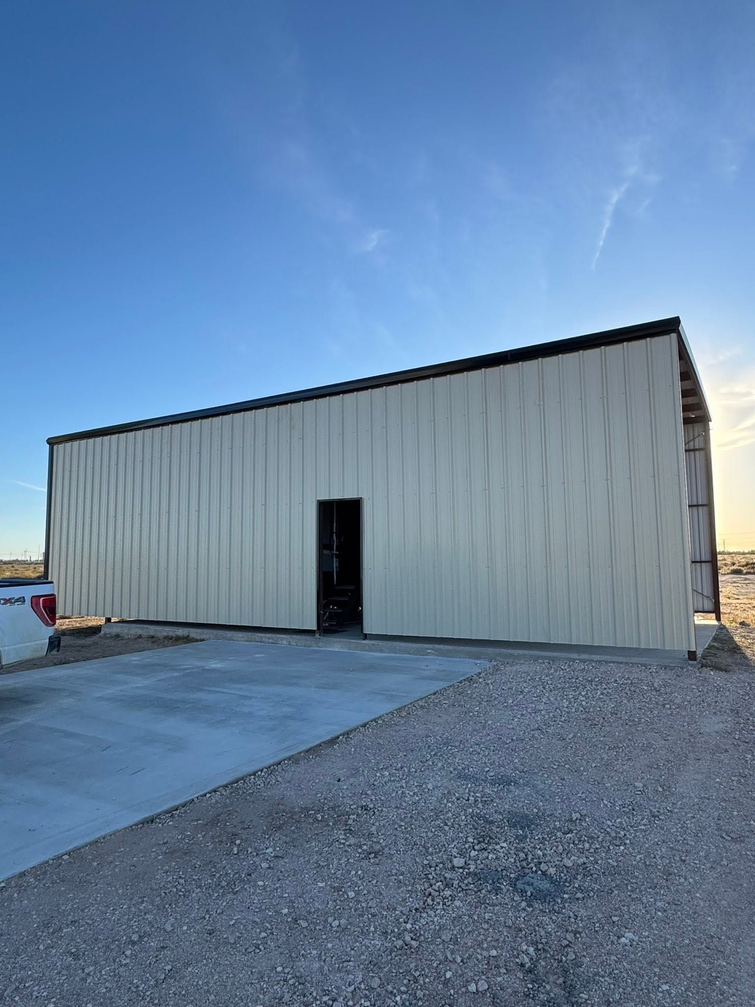 Metal industrial building with a dark doorway beside a gravel lot under a clear blue sky