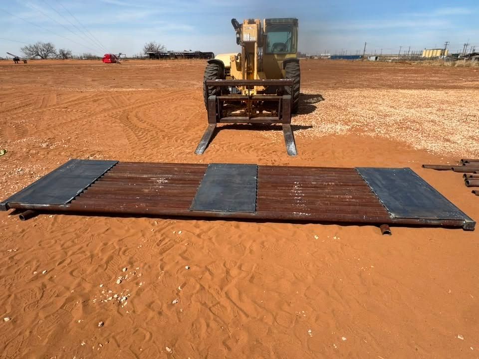 Bulldozer approaching a portable black ramp on a red dirt field under a clear sky
