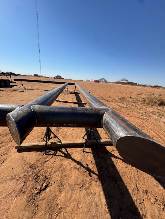 Long metal pipe on dry dirt field under a clear blue sky, viewed from the ground