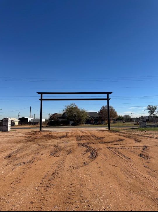 Rural dirt road beneath a black wooden gate frame under a clear blue sky