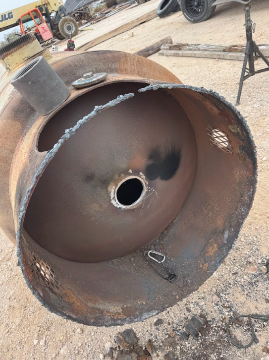 Rusty metal wheel rim lying on dirt, with a cracked inner edge and central hole at a work site.