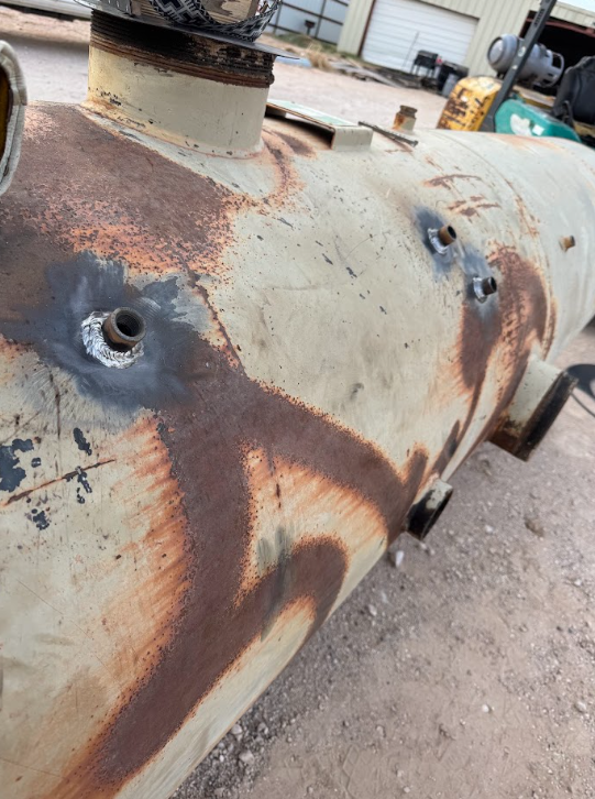 Rusty cylindrical metal tank with valves and heavy corrosion outdoors