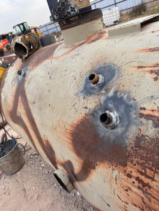 Rusty cylindrical tank with two welded nozzles in an industrial yard