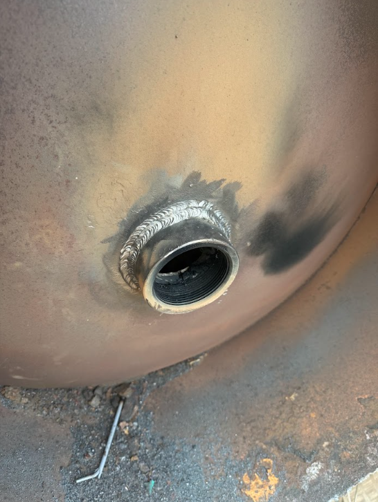 Close-up of a rusted metal tank with a circular opening and stained surface.