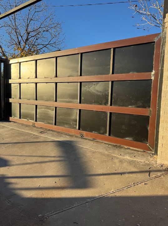 Brown metal garage door with dark panels in a driveway, lit by low sunlight