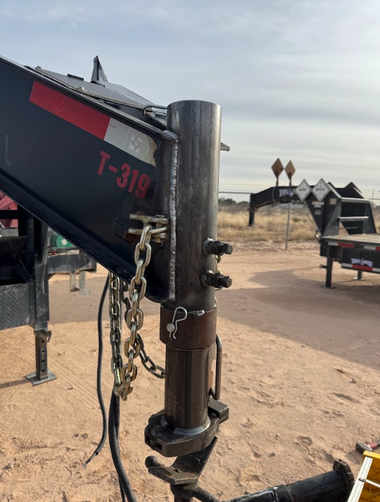 Close-up of a black trailer hitch with chains and red lettering in a dusty outdoor lot