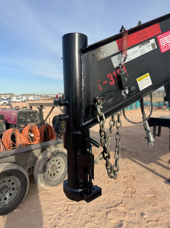 Black trailer-mounted hydraulic post in a dusty work yard, with chains and coiled orange hoses nearby