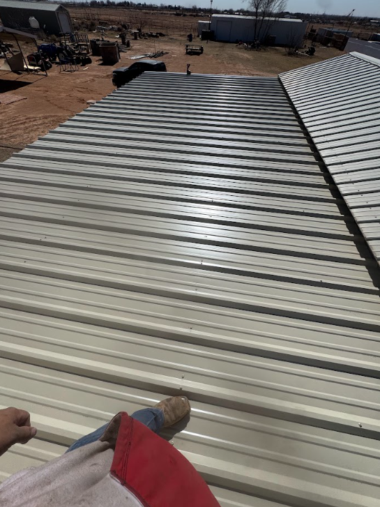 Hands using a tool on a corrugated metal roof in a dusty industrial yard.