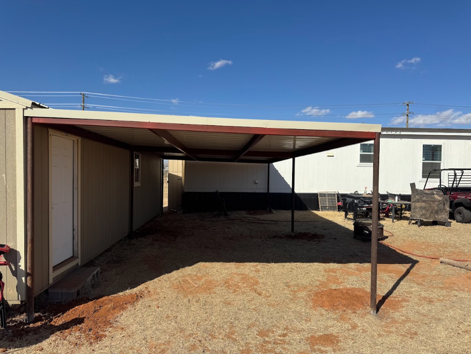 Empty gravel lot beside a white building with a metal carport under a blue sky