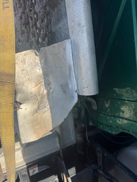 Close-up of a metal gutter and pipe beside a green wall, with a yellow strap in the foreground.