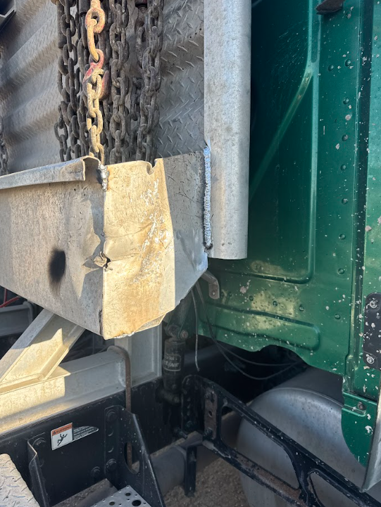 Close-up of a truck’s rear corner with a chain, yellow block, and green metal side panel.