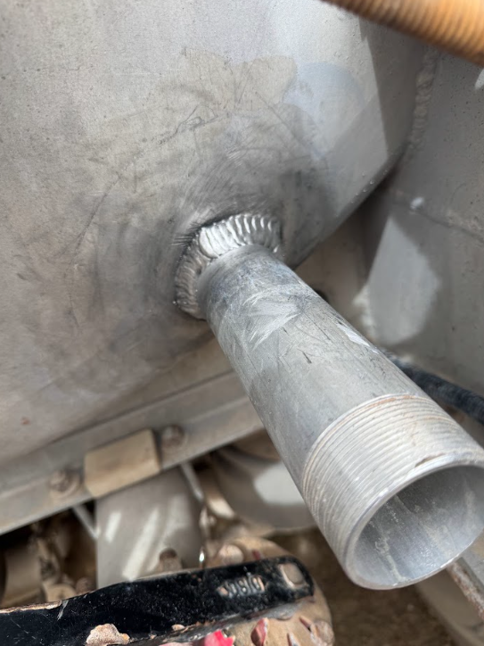 Close-up of a metal tube welded to a gray industrial surface.