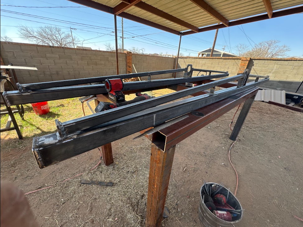 Black metal beams on wooden supports under a shed, with a red clamp and desert background