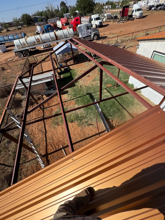 Rooftop view of metal beams and corrugated sheets at a construction site, with trucks and workers below