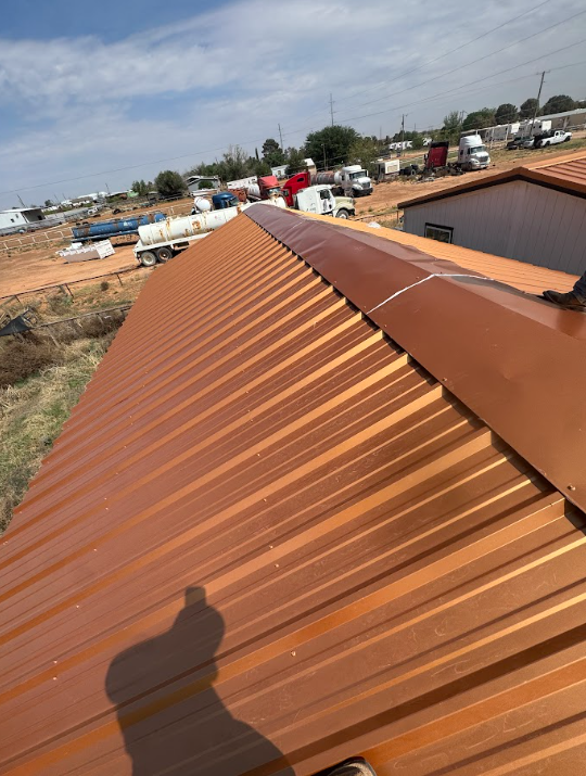 Brown metal roof on a building under construction, viewed from above with a shadow in the foreground