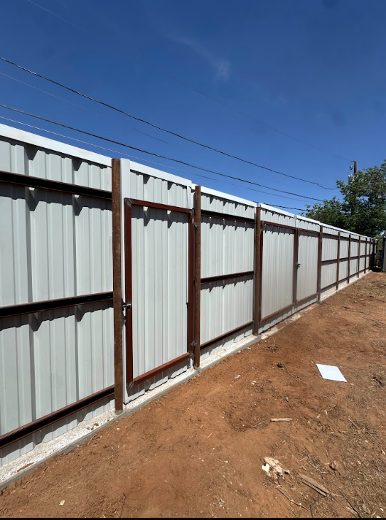Long corrugated metal fence along a dirt path under a clear blue sky