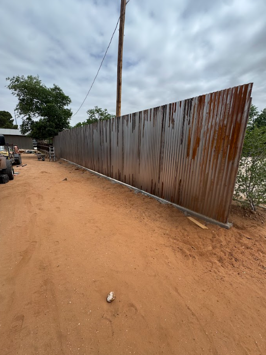Rusty corrugated metal fence along a dirt road under a cloudy sky