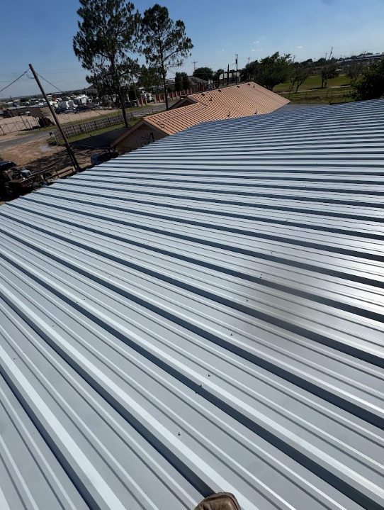 Corrugated metal roof with trees and a sandy yard in the background