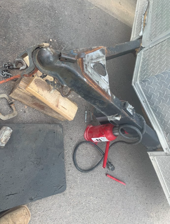 Black metal hitch arm attached to a trailer, with a red tool on the ground nearby.