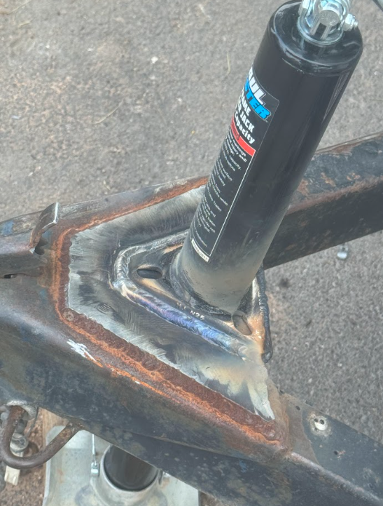 Welded metal trailer hitch mount with a black jack post on pavement