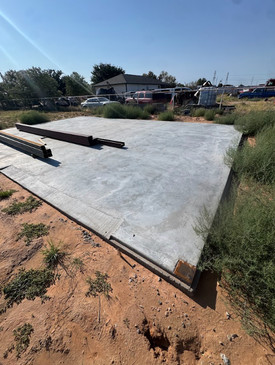 Concrete foundation slab under construction with anchor bolts and rebar in a grassy lot