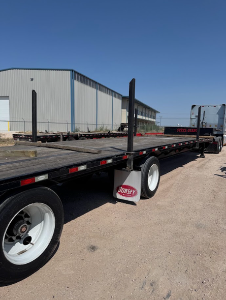 Black flatbed trailer parked beside a metal warehouse under a clear blue sky.