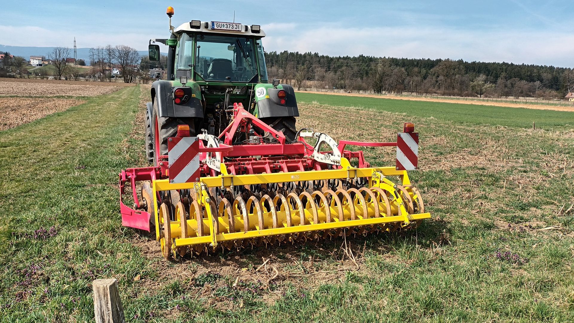Ein Traktor mit einer gelb-roten Maschine pflügt ein Feld.