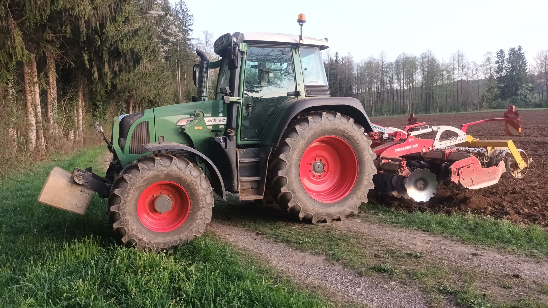 Ein grüner Traktor mit roten Rädern pflügt ein Feld.