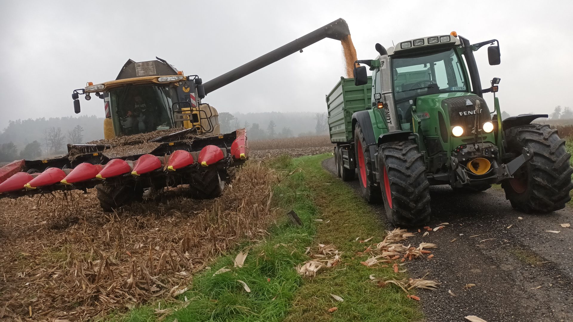 Ein grüner Traktor fährt neben einem Mähdrescher auf einer Straße her.
