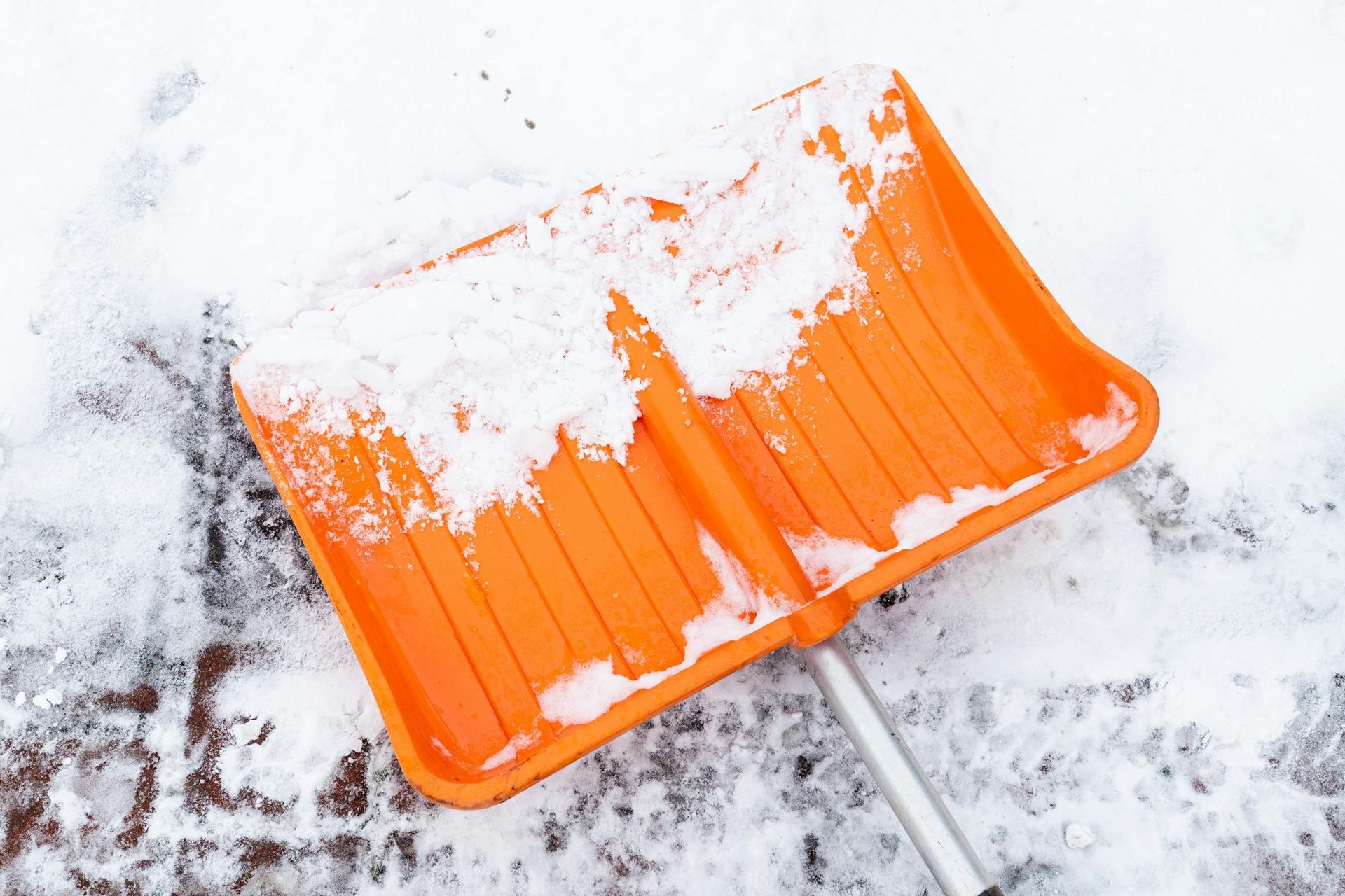 Eine orangefarbene Schneeschaufel liegt mit Schnee bedeckt auf dem Boden.