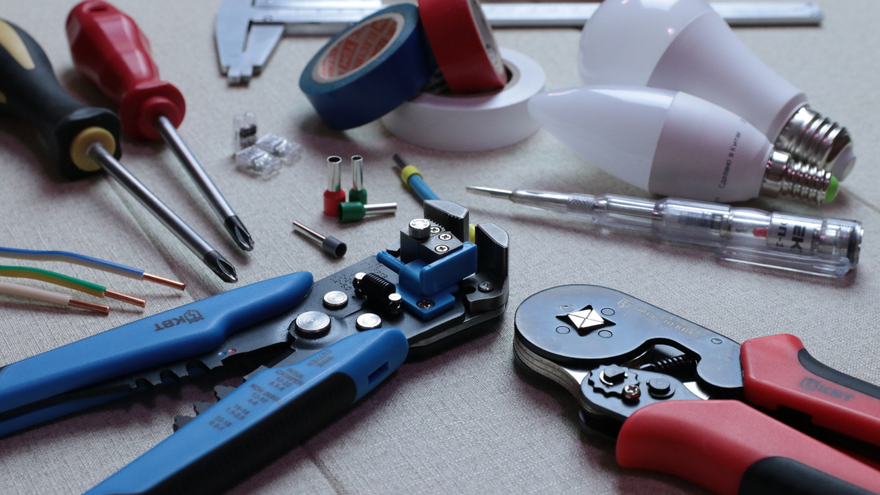 Assorted electrical tools and components on a workbench, including wire strippers, screwdrivers, plugs, and bulbs