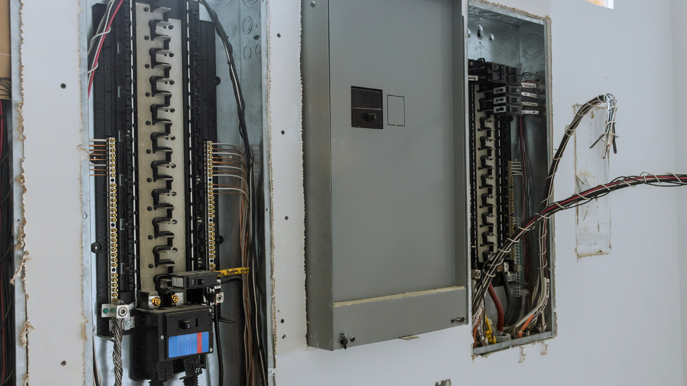 Open electrical breaker panels and wiring on a wall, with one panel door hanging open.