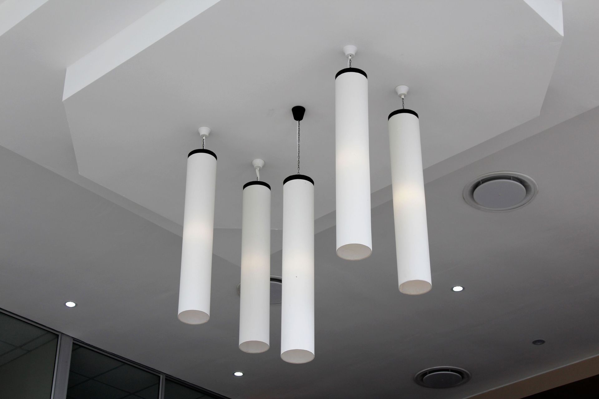 Modern ceiling with five white cylindrical pendant lights hanging in a row