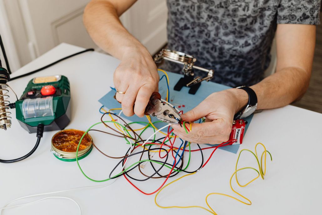 Person soldering colorful wires on a tabletop with electronics tools and components.