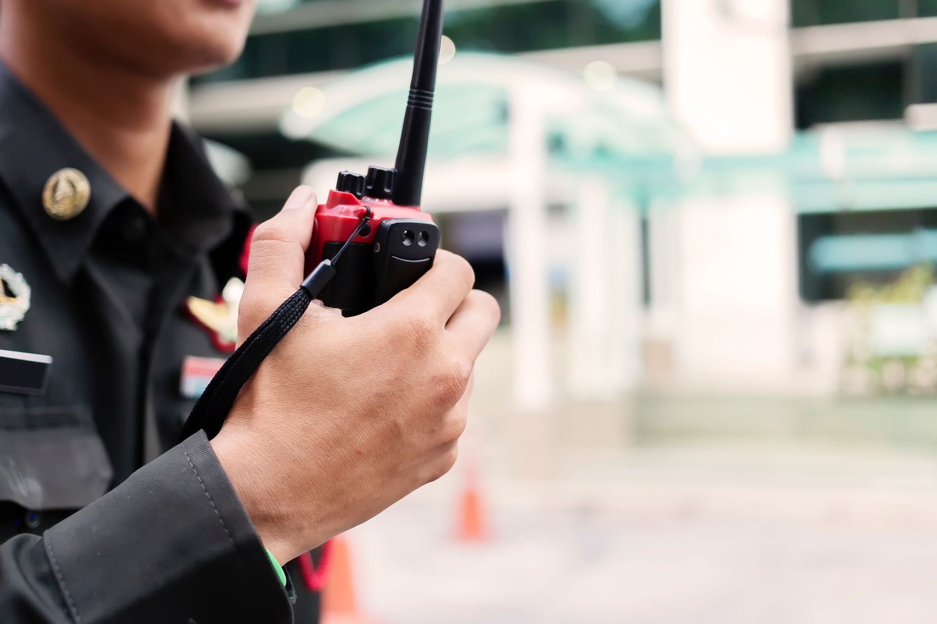 Security personnel holding a two-way radio while monitoring an outdoor commercial property. Security personnel holding a two-way radio while monitoring an outdoor commercial property.